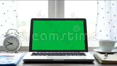 4K. 笔记本电脑，带有绿色屏幕色键，放在靠近窗户的办公桌上，并有白色窗帘吹过